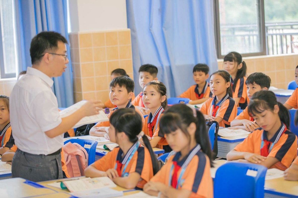 A teacher speaking to a class of primary school children at their desks