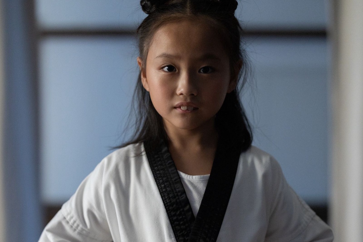 A young girl in a white taekwondo uniform tying her belt in a studio