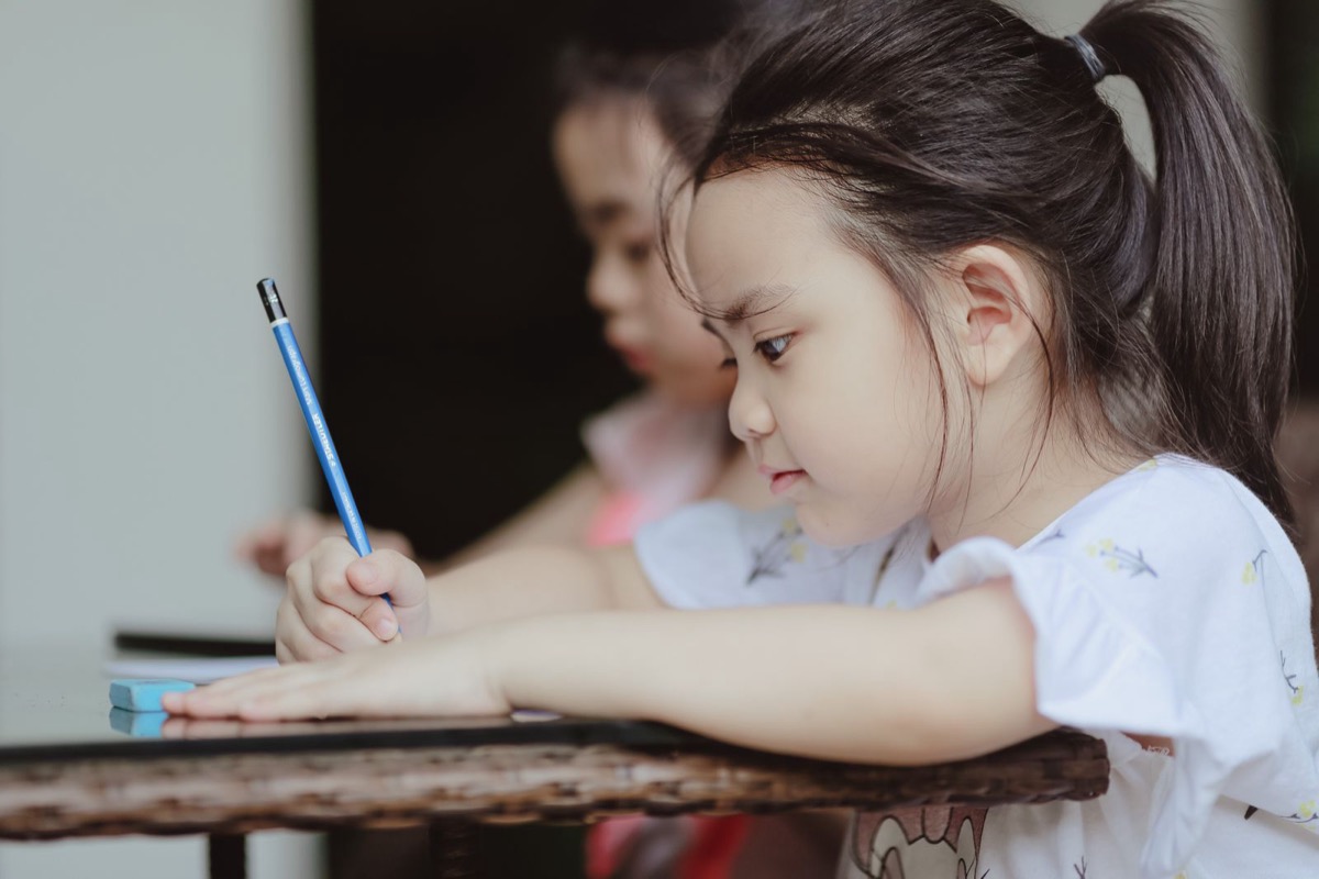 A young girl concentrating as she draws with a pencil at a table