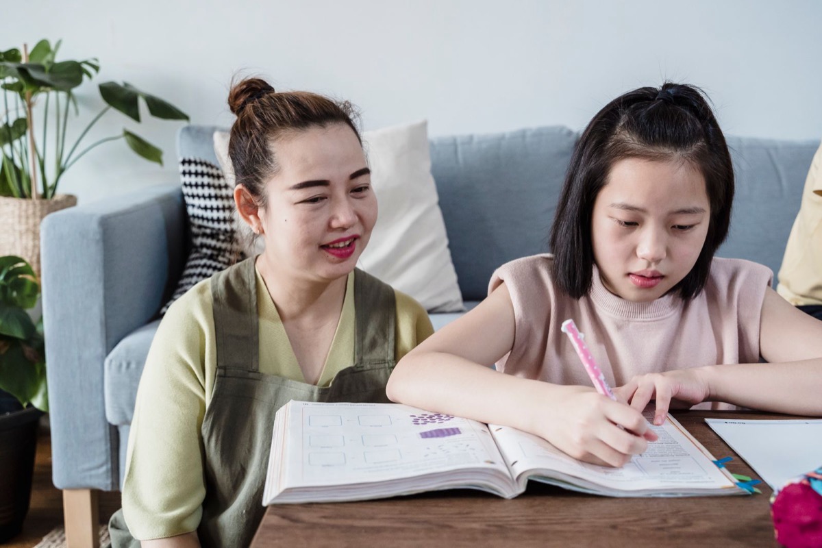 A mother sitting beside her daughter as she works through a workbook at home