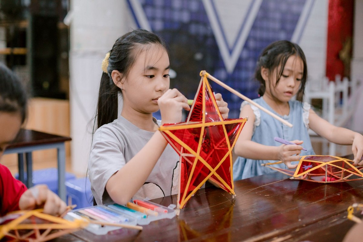 Two children making paper lanterns at a craft table in a community hall