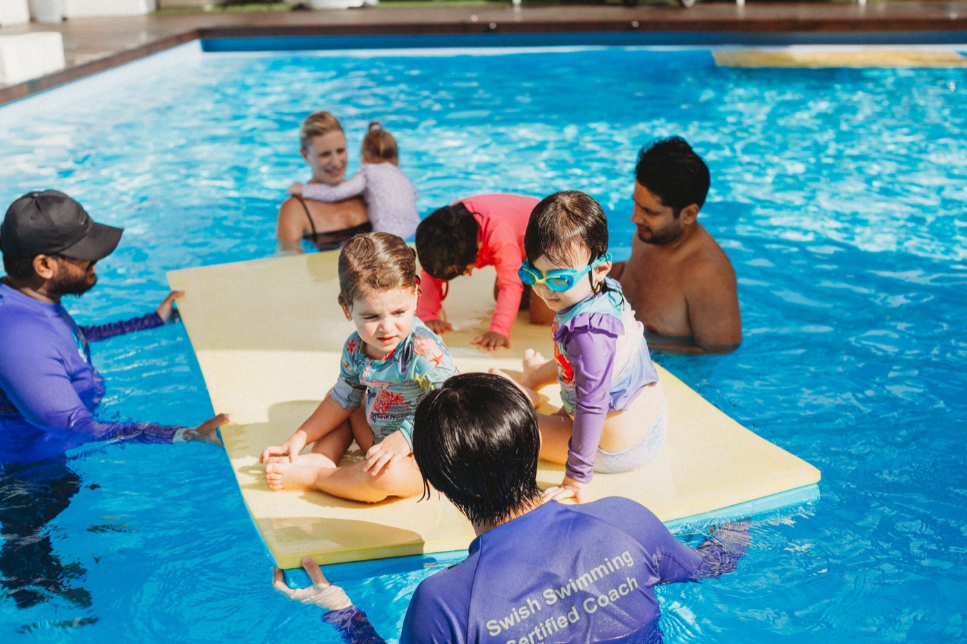 Toddler classes add the skills that matter around a pool: jumping in to you, turning back to the wall, holding on and climbing out. You still get in. Most schools keep a parent in the water until 3 or later, and SWISH! keeps you in until 3.5.