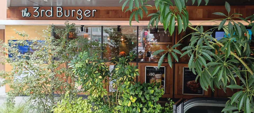 the 3rd Burger 新宿大ガード店の外観。看板の周りに緑の植栽が並ぶ