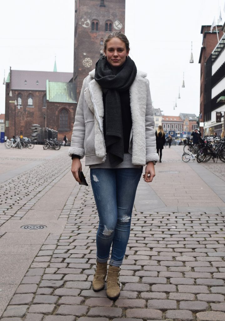 Street style danois à Aarhus, femme avec des bottes beiges, jean devasé et une veste fourrée et une grosse écharpe noire.