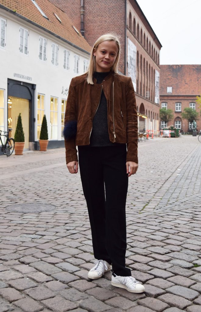 Street style danois à Aarhus, femme avec une veste en cuir, un pantalon de costume noire et des baskets blanches.