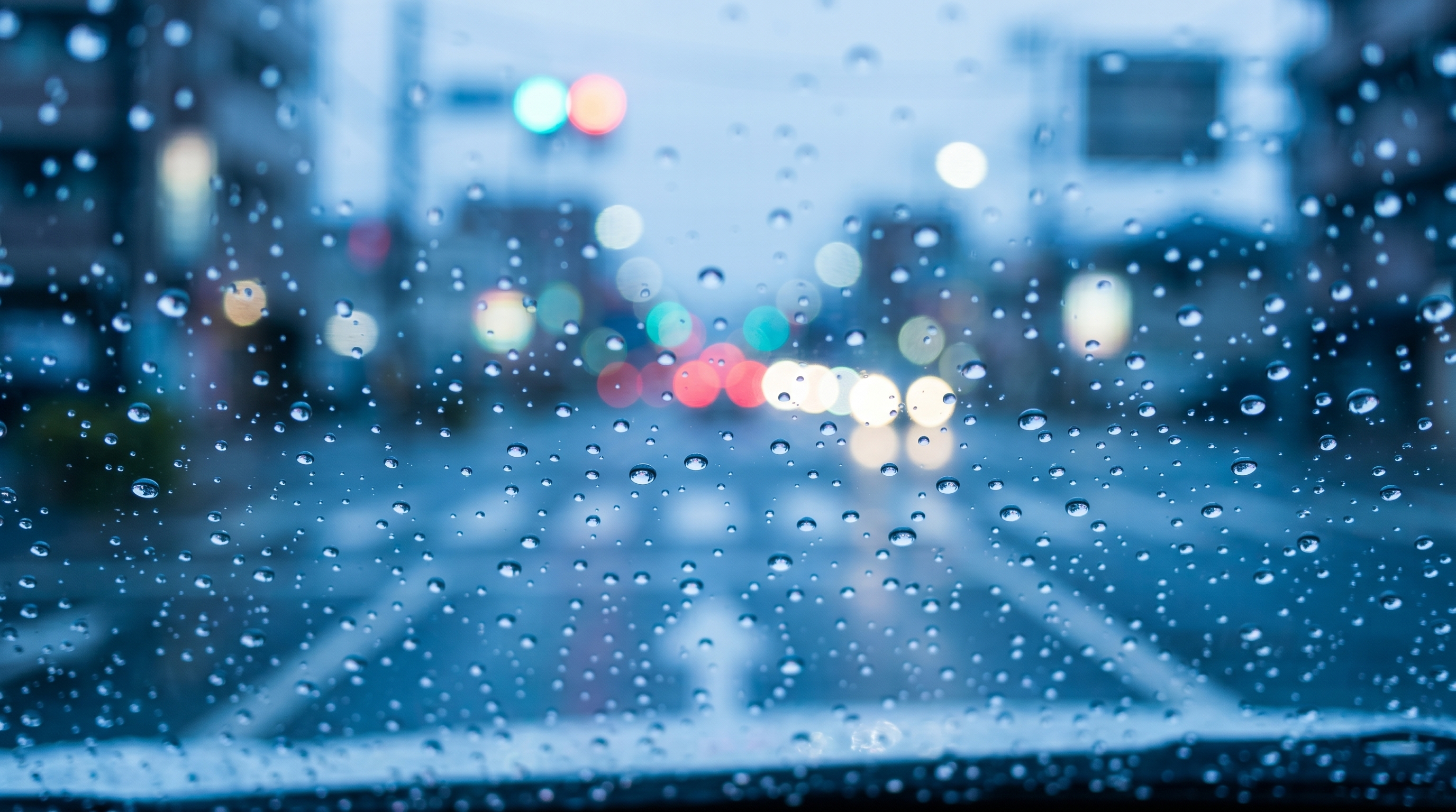 車のフロントガラスに当たった雨粒が丸い水滴となって弾かれているクローズアップ写真。背景の美しい玉ボケとともに、強力な撥水効果とクリアな視界が伝わる雨天の様子。