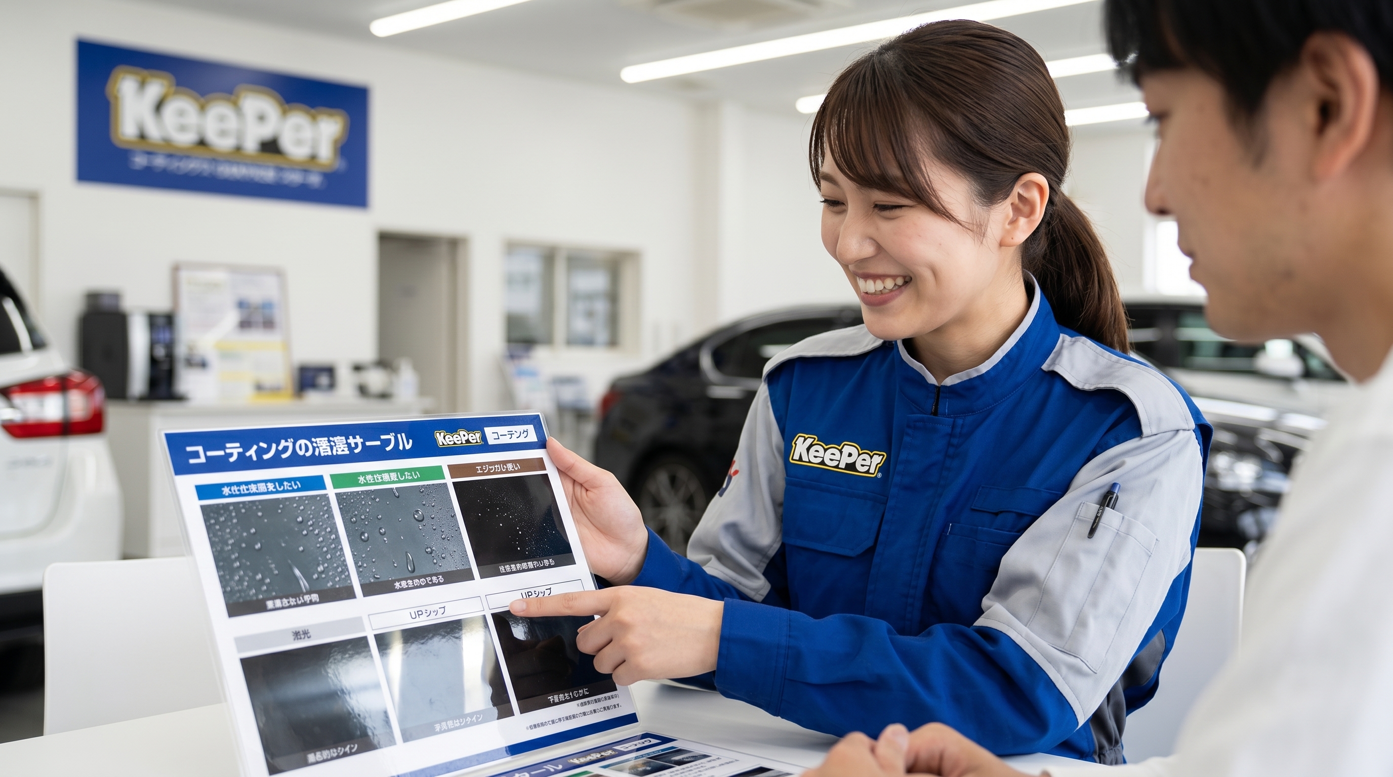 制服を着た女性スタッフが、テーブル越しにお客様へ車のコーティング用サンプルパネルを指差して丁寧に説明しているシーン。リラックスした安心感のある接客の様子です。