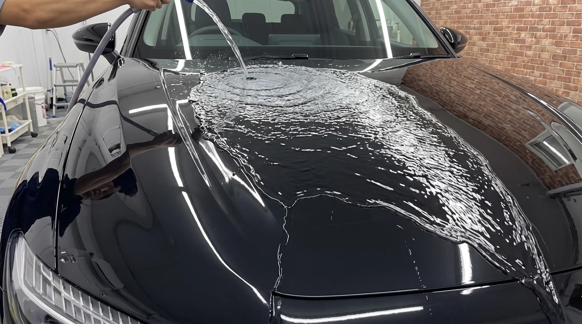 黒い車のボンネットに水をかけた際、水玉にならずにシート状になってスムーズに滑り落ちていく、親水性や滑水性の特徴を分かりやすく捉えた表面のクローズアップ。
