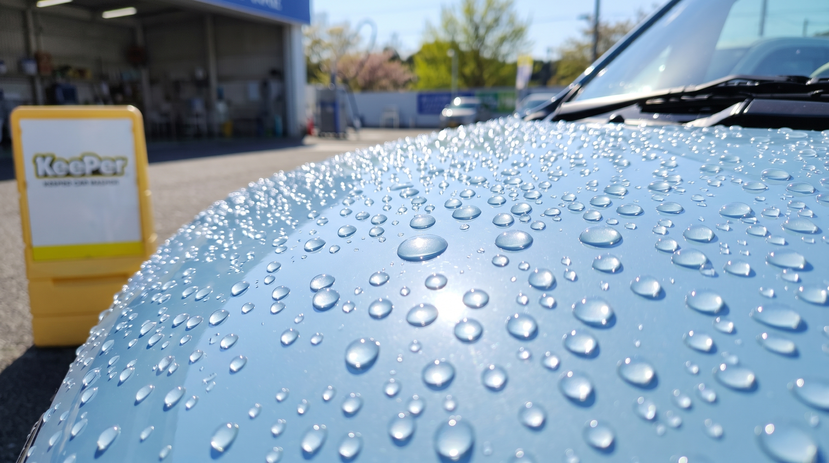 雨上がりの屋外で、パステルカラーの車のボンネットに弾く美しい球状の水玉のクローズアップ。太陽の光を反射してキラキラと輝く水滴を、明るく爽やかに捉えた様子です。