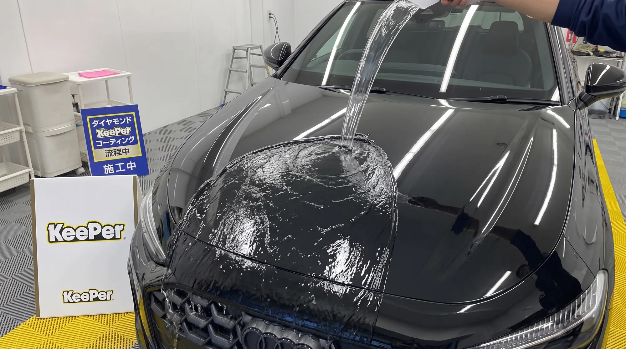 黒いSUVのボンネットに水をかけた際、水滴が水玉にならずにシート状になって滑り落ちていく、滑水性や親水性の特徴を表現したクローズアップ写真。