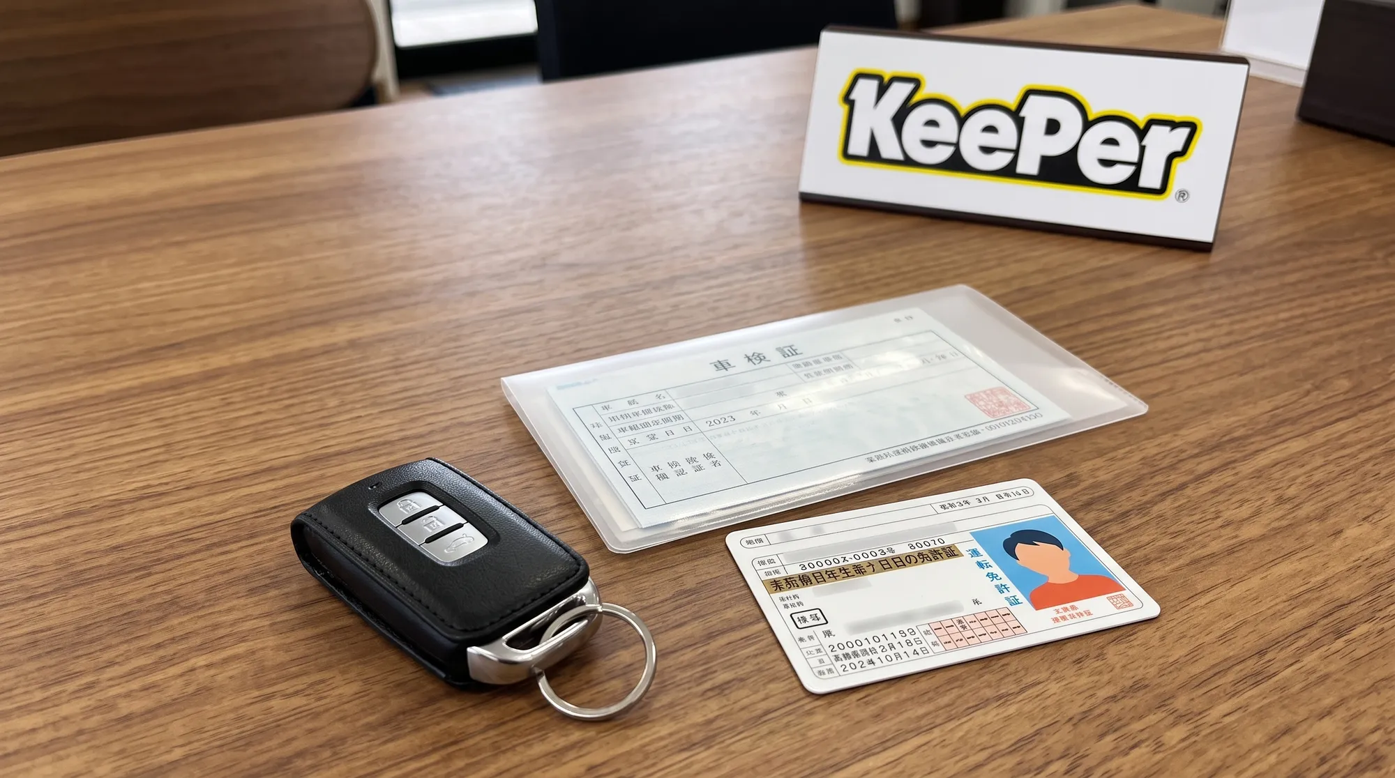 美しい木目のテーブルの上に、車のスマートキー、車検証が収納されたファイル、そして運転免許証が綺麗に整理されて置かれている様子。