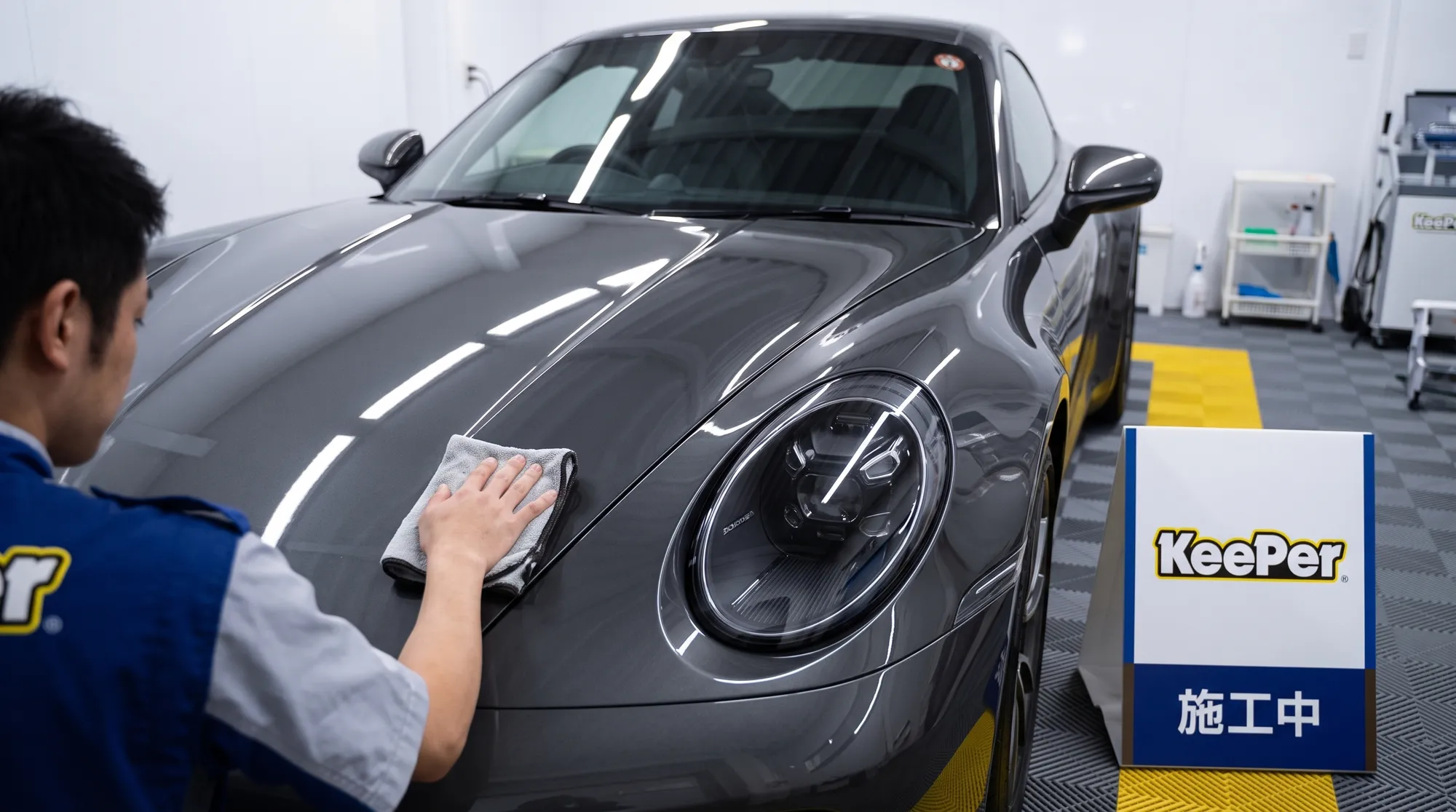 清潔で明るい施工ブースの照明が、コーティング施工を終えて磨き上げられた車のボディに艶やかに映り込んでいる様子。高級感のある落ち着いた色合いのクローズアップ画像。