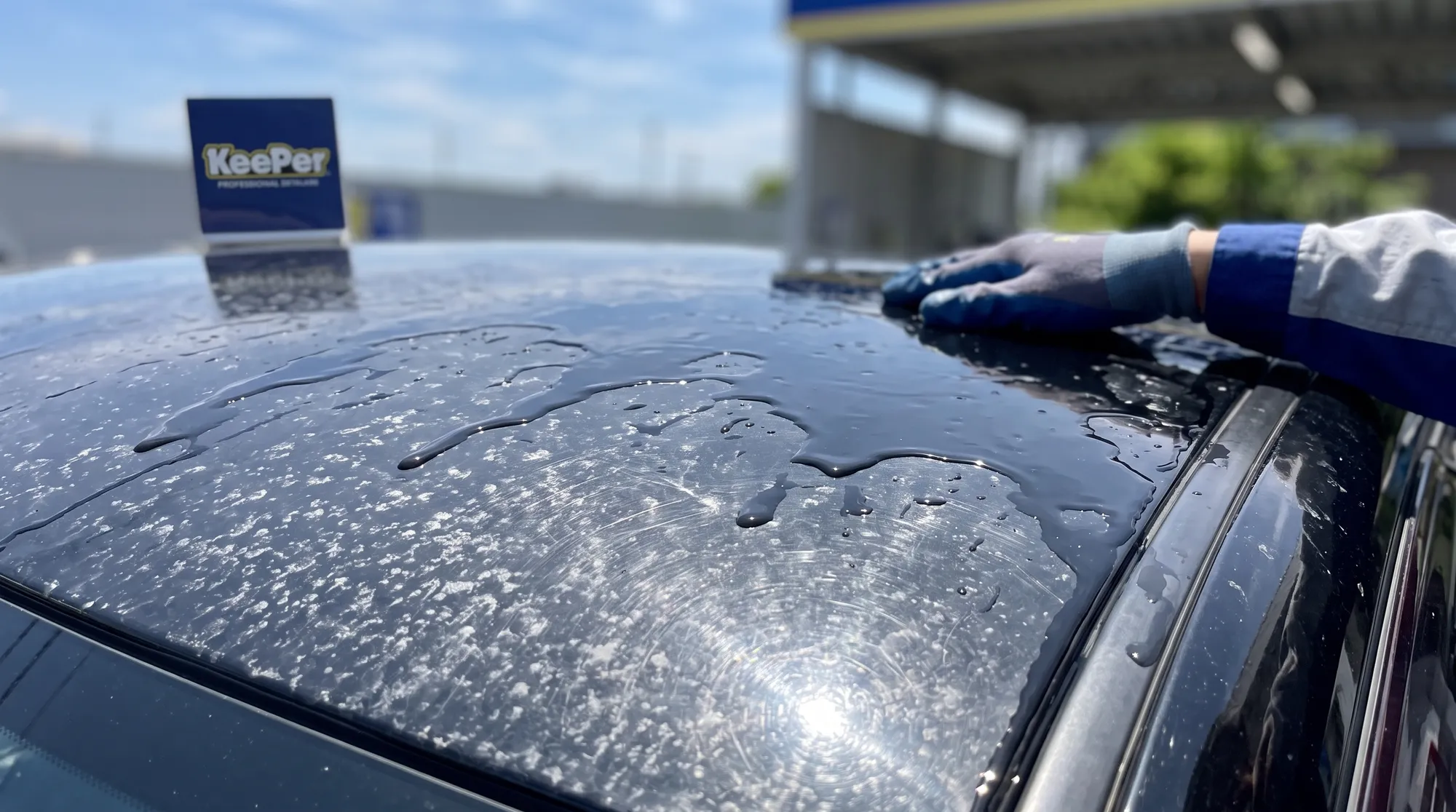 黒い車のルーフ部分を捉えたクローズアップ。劣化したコーティング表面に無数の水シミや洗車傷が付着し、撥水効果が落ちて雨水が潰れて不規則に広がっている様子。