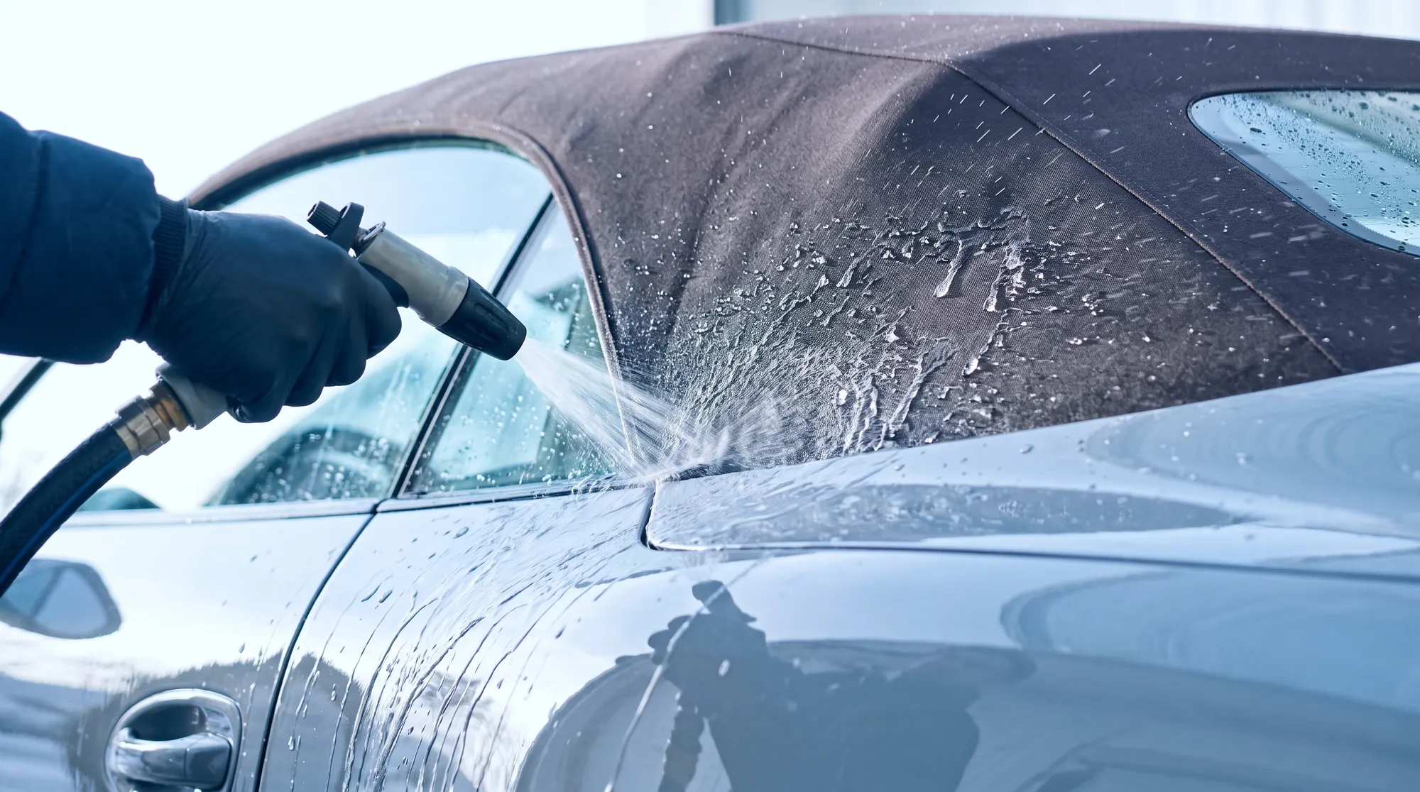 洗車を受けるオープンカーの様子。ボディと幌の境界部分に水がかけられ、ボディを水が滑り落ちる様子と幌が水を弾く様子が同時に見える、スタッフの手元のクローズアップ。