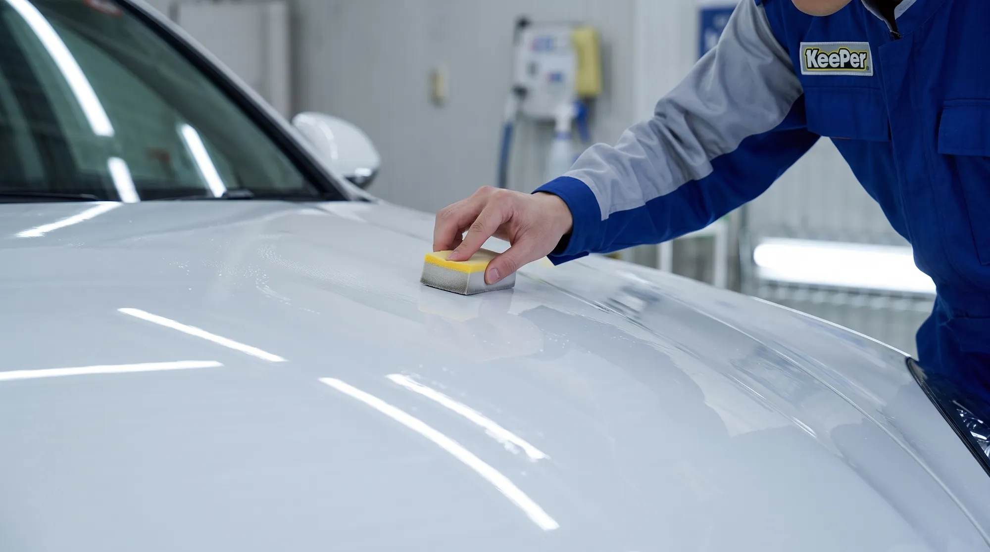 白い車のボディに専用スポンジでコーティング剤を塗り込むスタッフの手元
