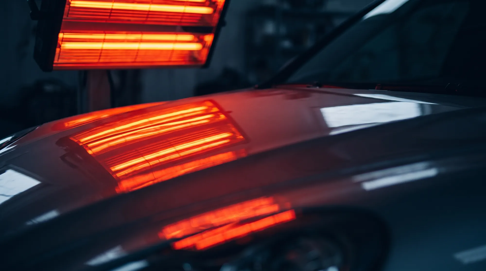 塗装直後の車のボンネットに、赤外線乾燥機の赤やオレンジ色に光るヒーター管が反射しているクローズアップ。コーティング前の塗装の乾燥と硬化プロセスの様子。
