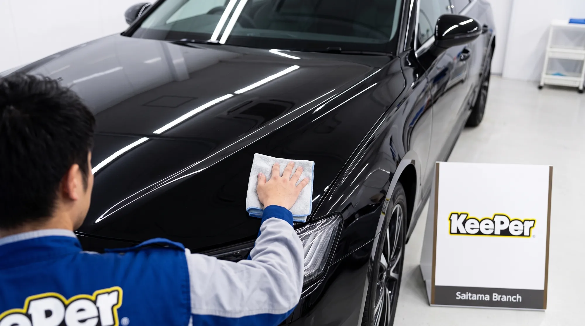 コーティング施工を終えて艶やかに仕上がった車のボディのクローズアップ画像。清潔なブースの明るい照明が磨き上げられた塗装に美しく映り込む、高級感あふれる様子。