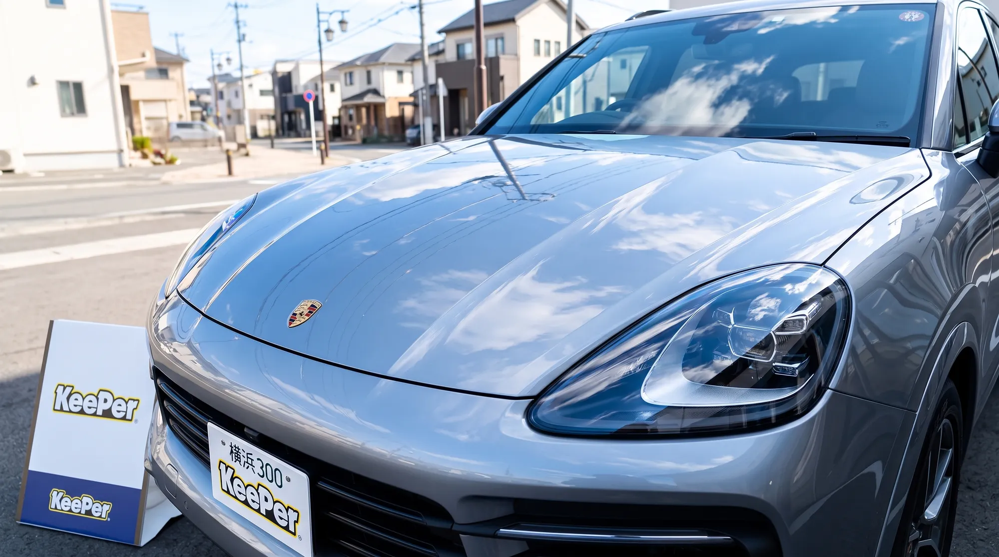 屋外の自然光の下、コーティング施工後の艶やかな車のボディに青空と街並みが美しく映り込んでいる画像。爽やかな色合いが塗装の美しい仕上がりを強調している様子。