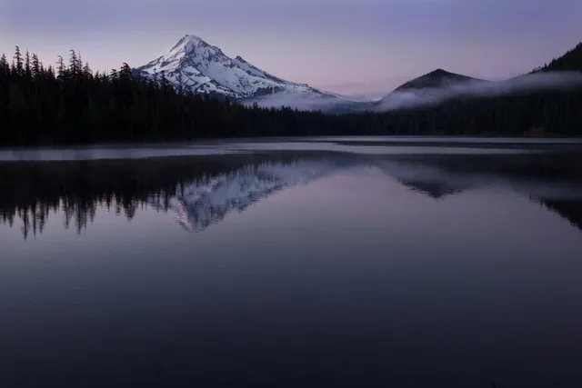 A still mountain lake reflecting snow-capped peaks at dawn