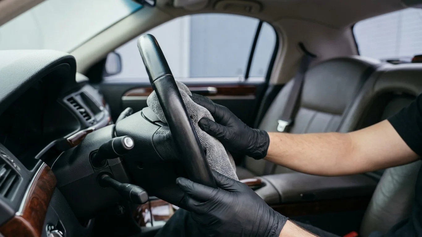 Hands in gloves carefully cleaning the steering wheel of a limousine.