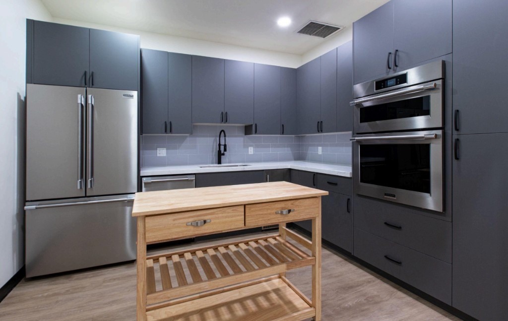 Modern reception kitchen with gray cabinetry, stainless steel appliances, and a wooden island at Bunker Family Funerals.