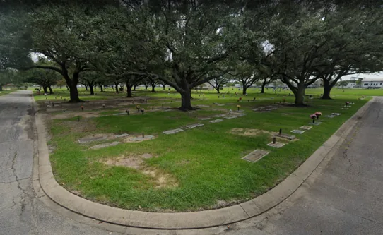 A grassy lawn-crypt garden beneath mature oaks at Memory Gardens Cemetery