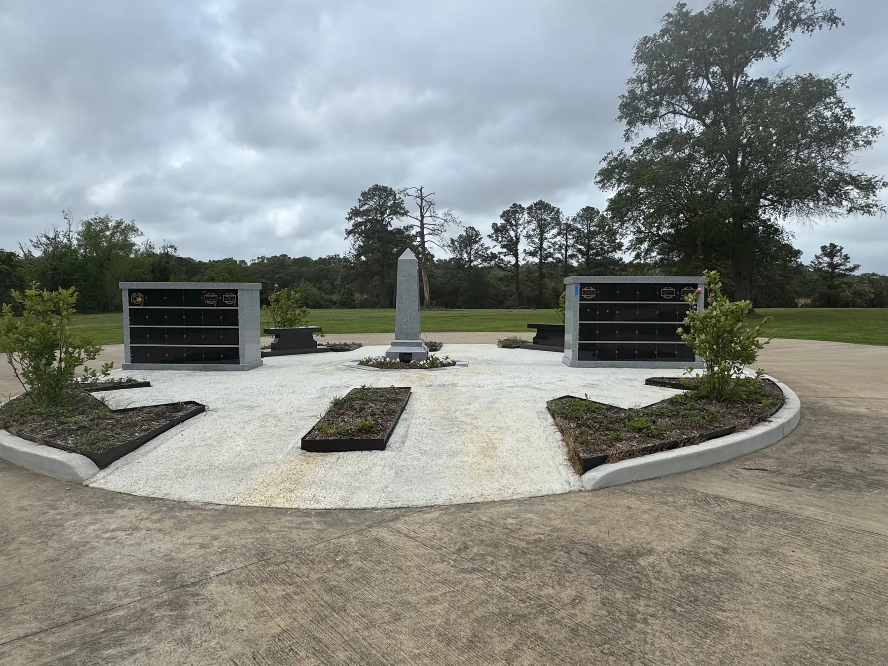 Cremation garden with columbaria and obelisk under a cloudy sky at Oak Bluff Memorial Park