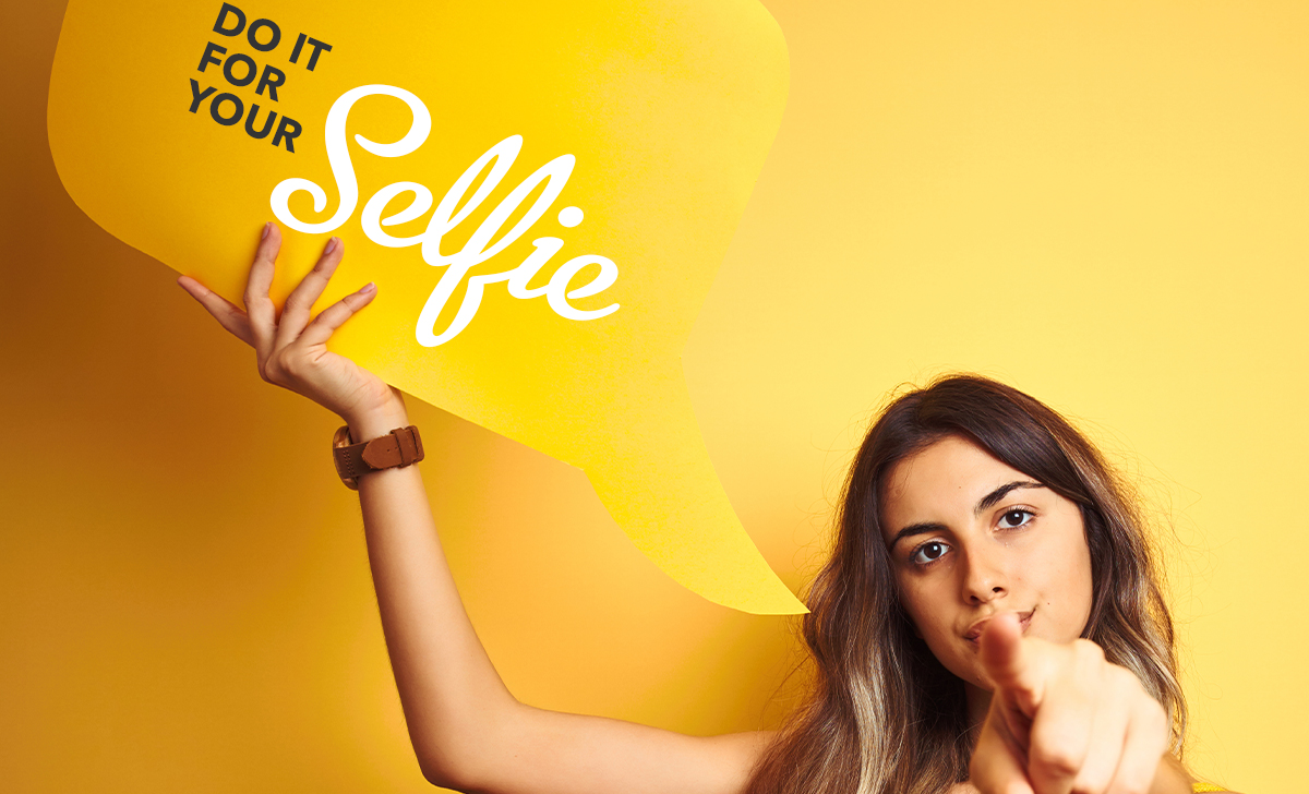 Girl holding speech bubble sign saying 'Do it for your selfie'