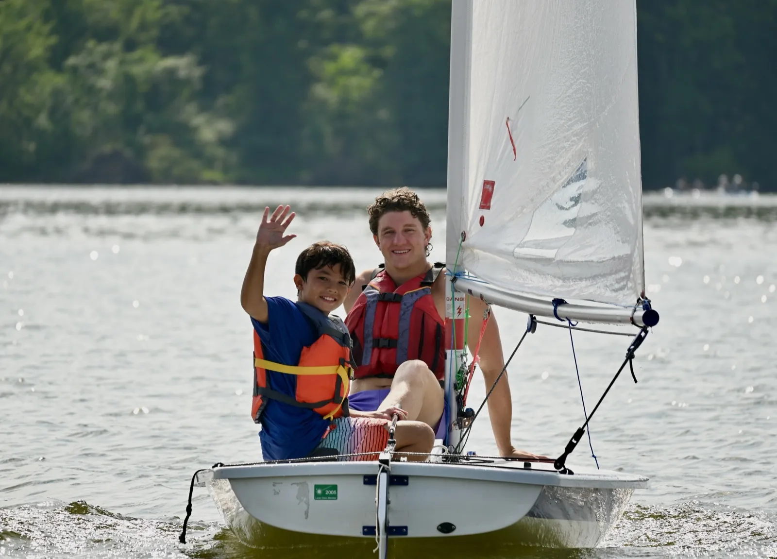 Instructor and waving camper smiling in a sunlit sailing dinghy