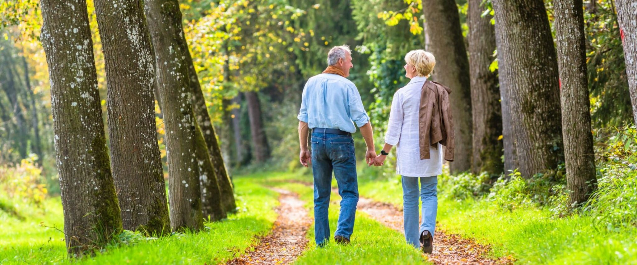 A senior couple holds hands while walking in nature together