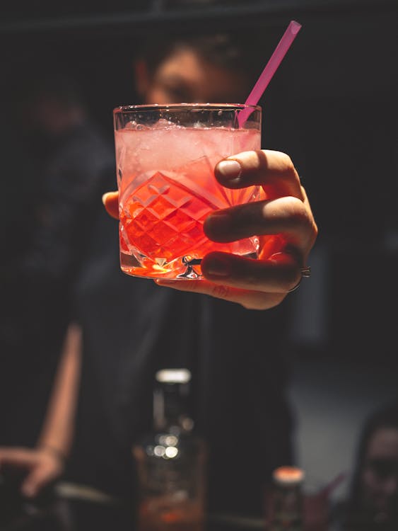 Free Man Holding Forward A Glass Of Iced Pinkish Colored Cocktail With A Straw Stock Photo