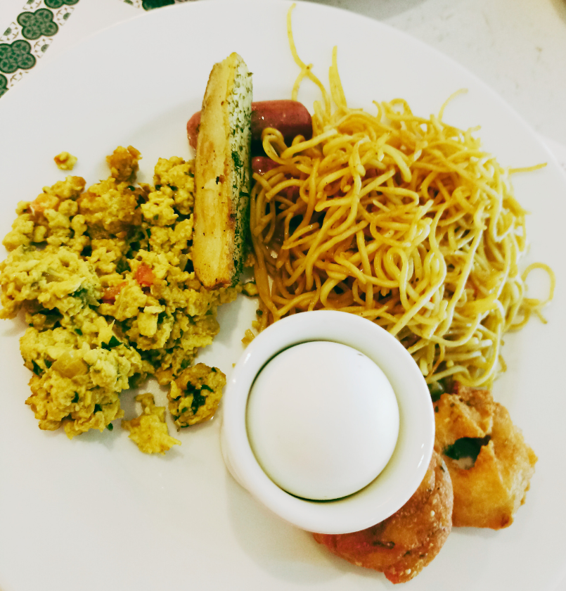 A hotel breakfast plate of noodles, egg bhurji and a small bowl of curry