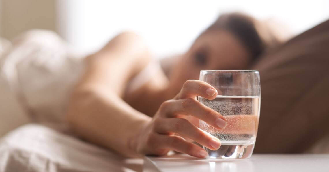 Young woman reaching for a glass of water in bed