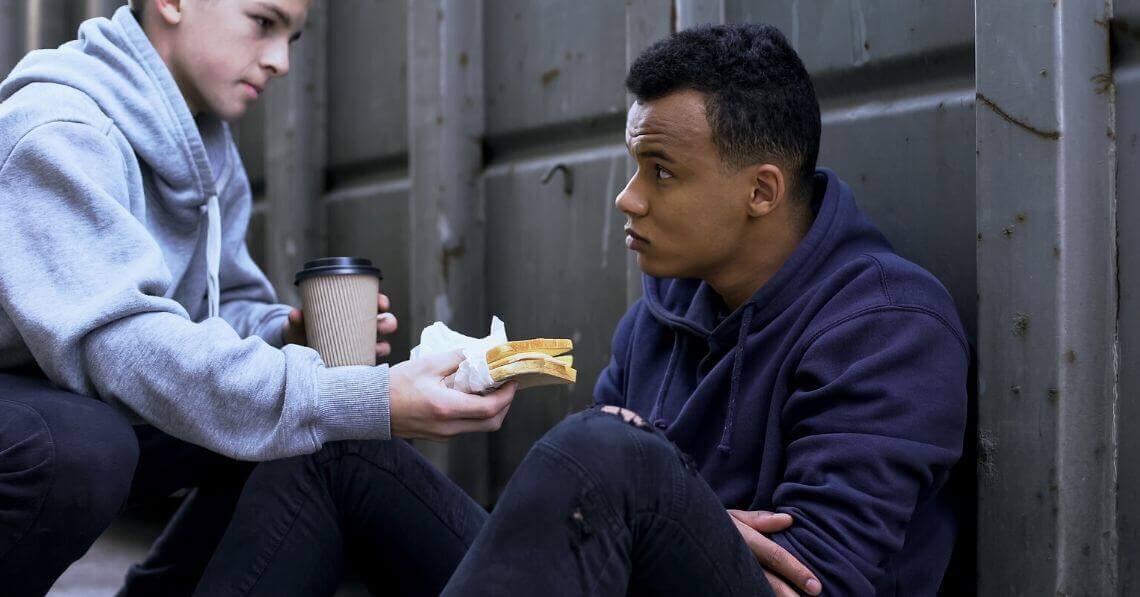 A young man giving a sandwich and a cup of coffee to a homeless man