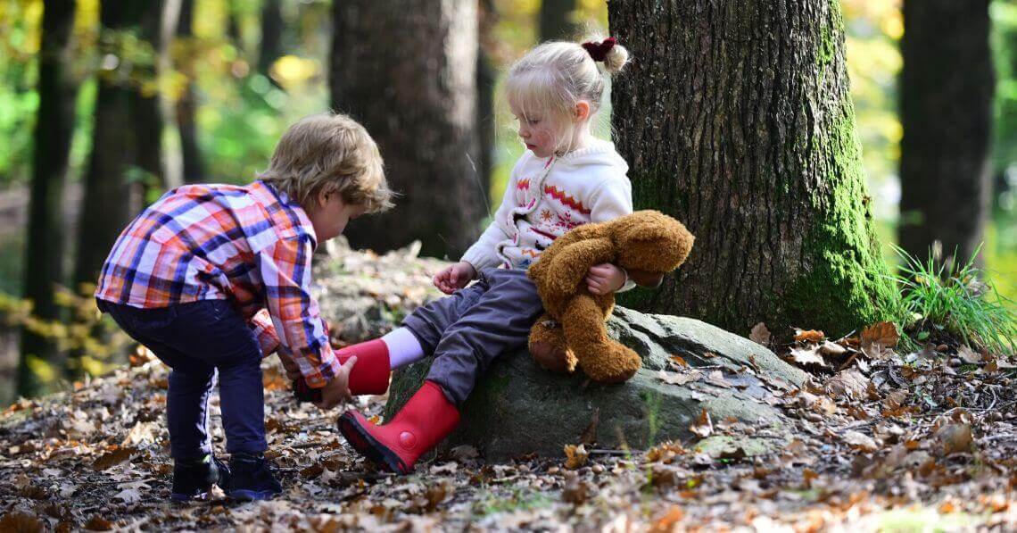 A toddler boy helping a toddler girl with her boots