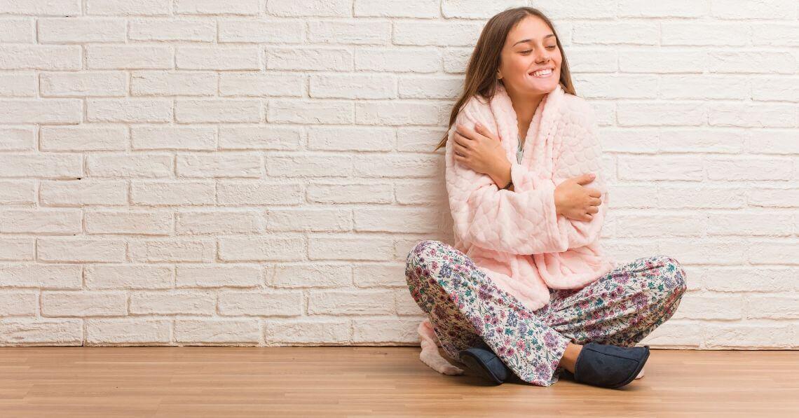 Cozy young woman sitting crossed leg, hugging herself