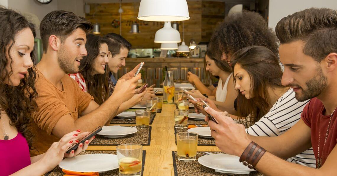 Young people at dinner table looking at their phones