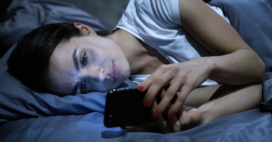 Young woman checking social media instead of sleeping