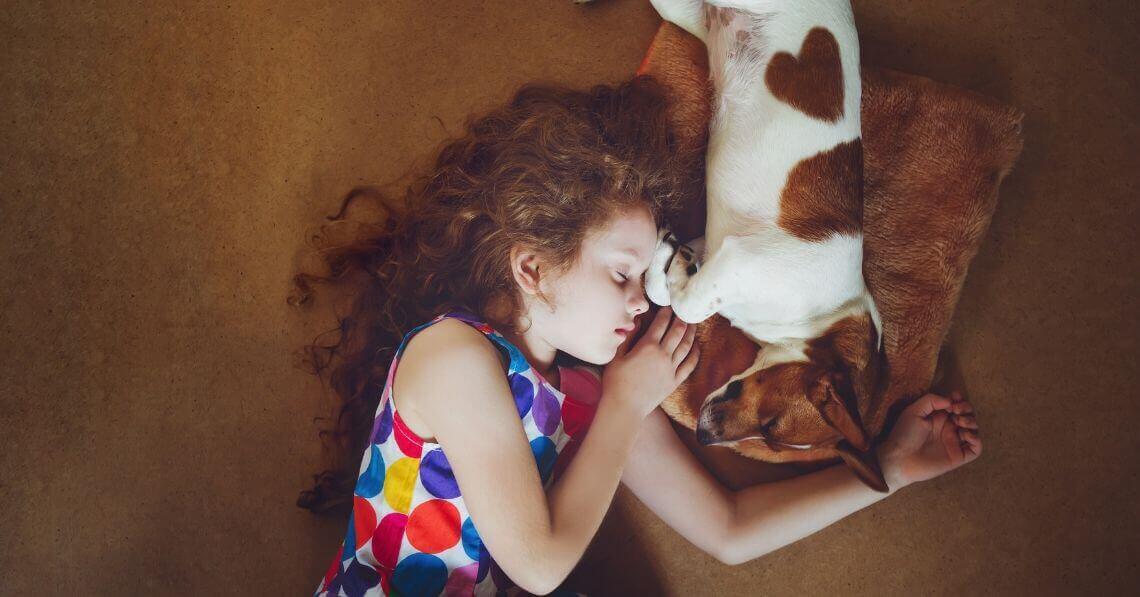 A toddler girl snggling with a dog on the carpet