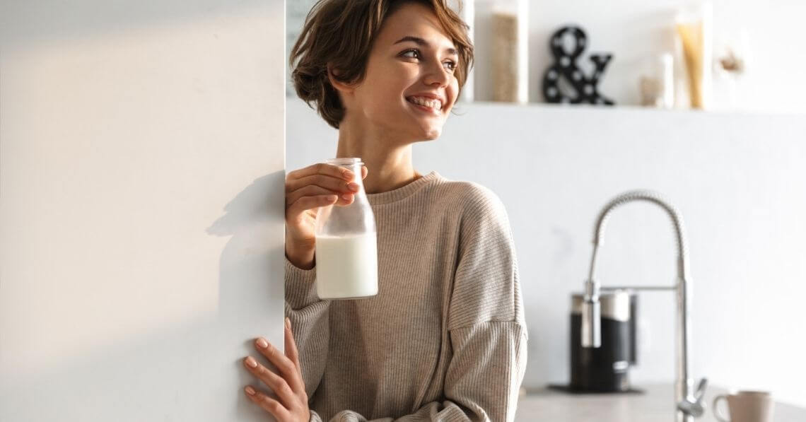 Young woman taking a bottle of plant milk from the fridge