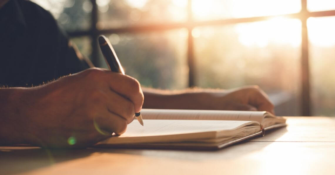 Close up of a man's hand holding a pen over a gratitude journal