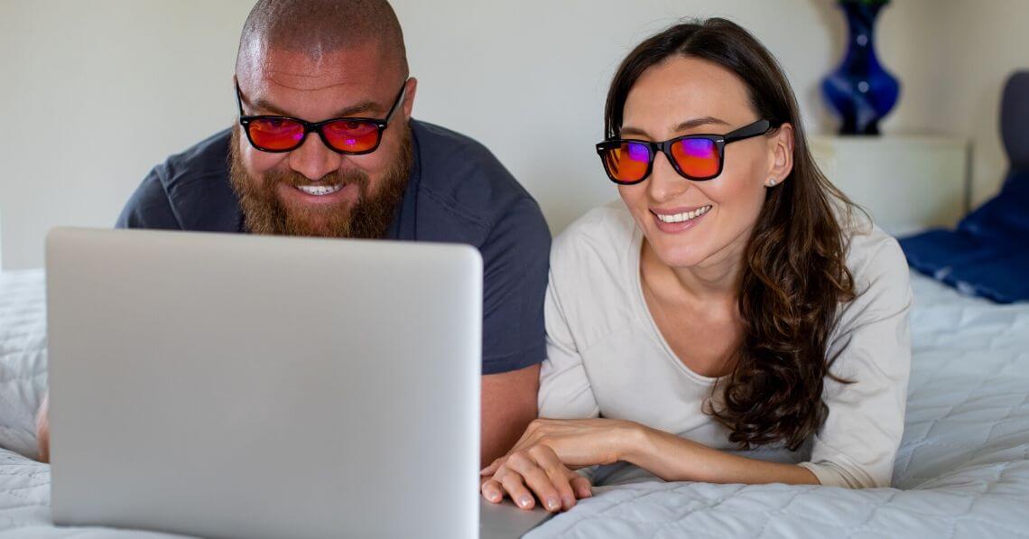 A couple sharing a laptop wearing blue light blocking glasses