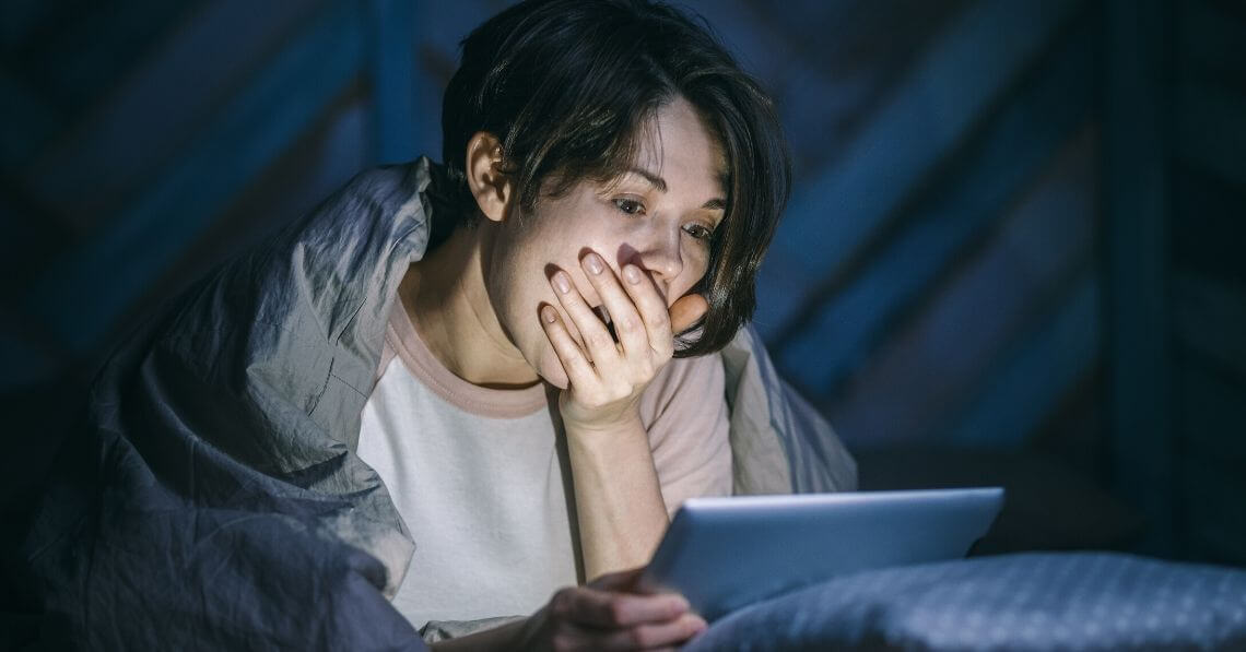 A person yawning while using their tablet late at night