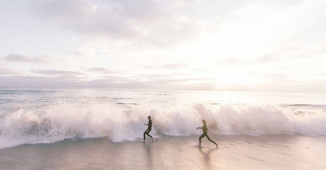 A couple in wetsuit running into the waves