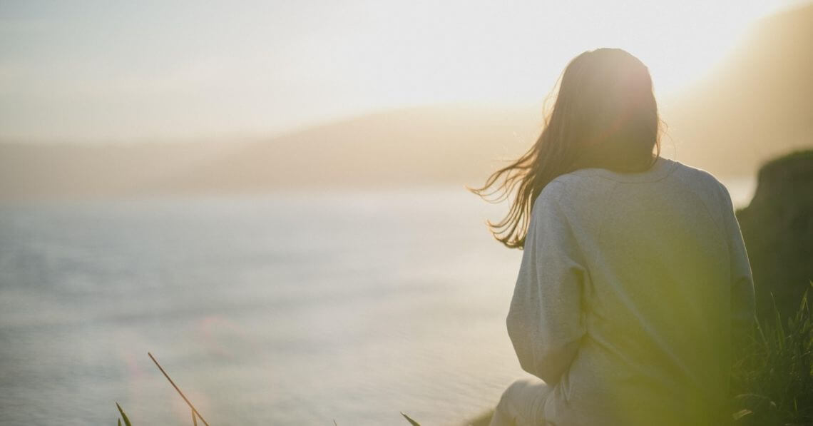 A woman over the cliffs of a beach watching the sunset