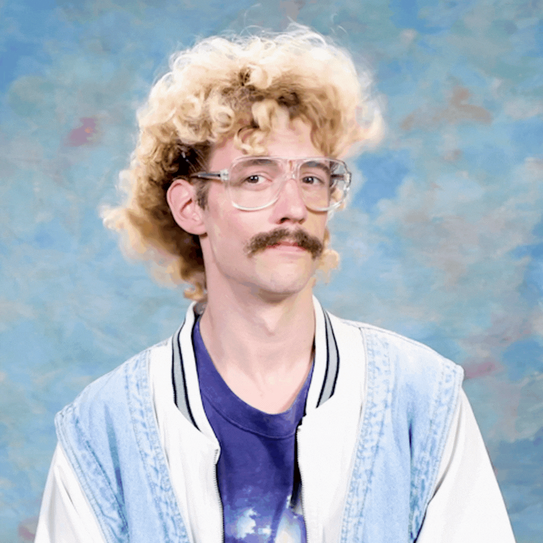  A portrait of a man with curly blonde hair and a mustache, wearing glasses and a vintage jacket, against a painted backdrop.
