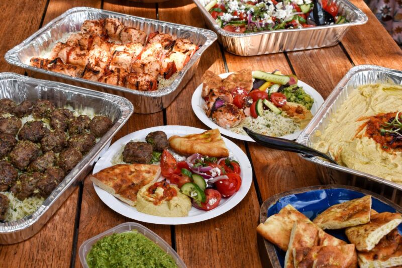 Assortment of menu items from Aba Catering, featuring trays of kebabs, salads, and hummus