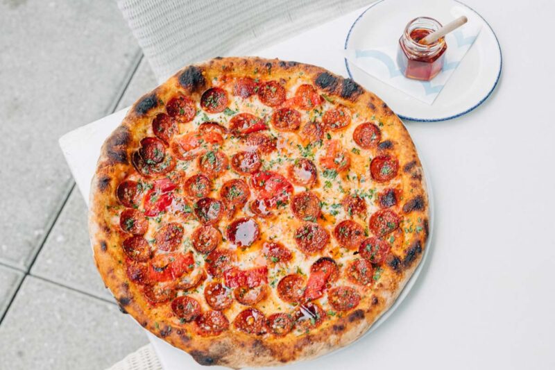 beautiful pepperoni pizza with small glass jar of spicy honey on the side