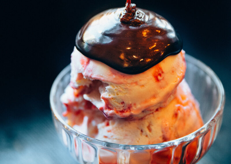 two stacked ice cream scoops with fudge in a glass cup