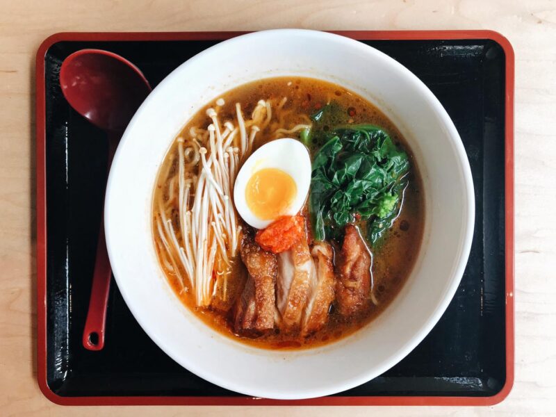 Bowl of yuzu ramen with eggs, meat, and vegetables in a bowl set on a black and red tray